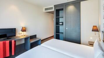 Una habitación de hotel moderna con una cama, un televisor, un escritorio con lámpara, un armario y una mesita de noche con lámpara.