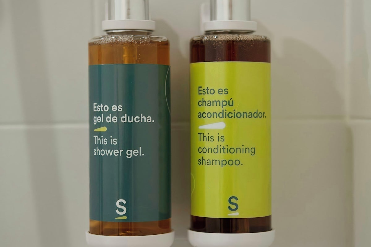 Deux bouteilles de gel douche et de shampoing après-shampoing sont posées sur un mur carrelé.