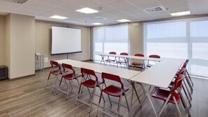 A conference room with a long table, red chairs, a whiteboard, and large windows.
