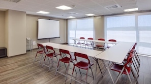 Un salón de conferencias con una larga mesa, sillas rojas, una pizarra y ventanas amplias.