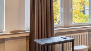 A modern room with a window, a table, an orange ottoman, and a radiator. - a&o Köln Hauptbahnhof (Cologne)