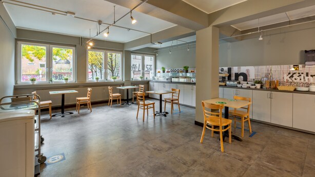 A spacious, well-lit kitchen area with modern appliances, ample seating, and large windows offering views of the outside. - a&o Köln Hauptbahnhof (Cologne)