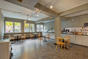 A spacious, well-lit kitchen area with modern appliances, ample seating, and large windows offering views of the outside. - a&o Köln Hauptbahnhof (Cologne)