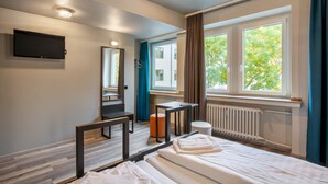A modern hotel room with a bed, a desk, a chair, a mirror, a TV, and a window with curtains. - a&o Köln Hauptbahnhof (Cologne)