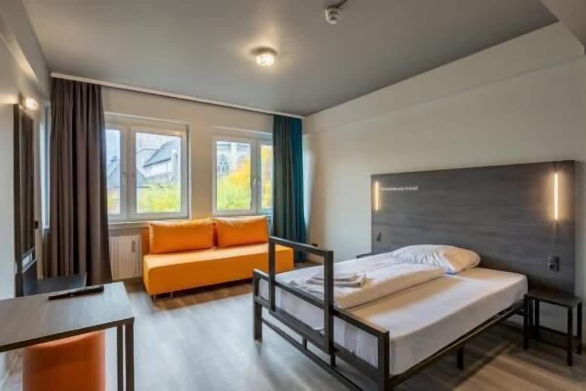 Una habitación de hotel moderna con cama, sofá, escritorio y vistas al exterior.