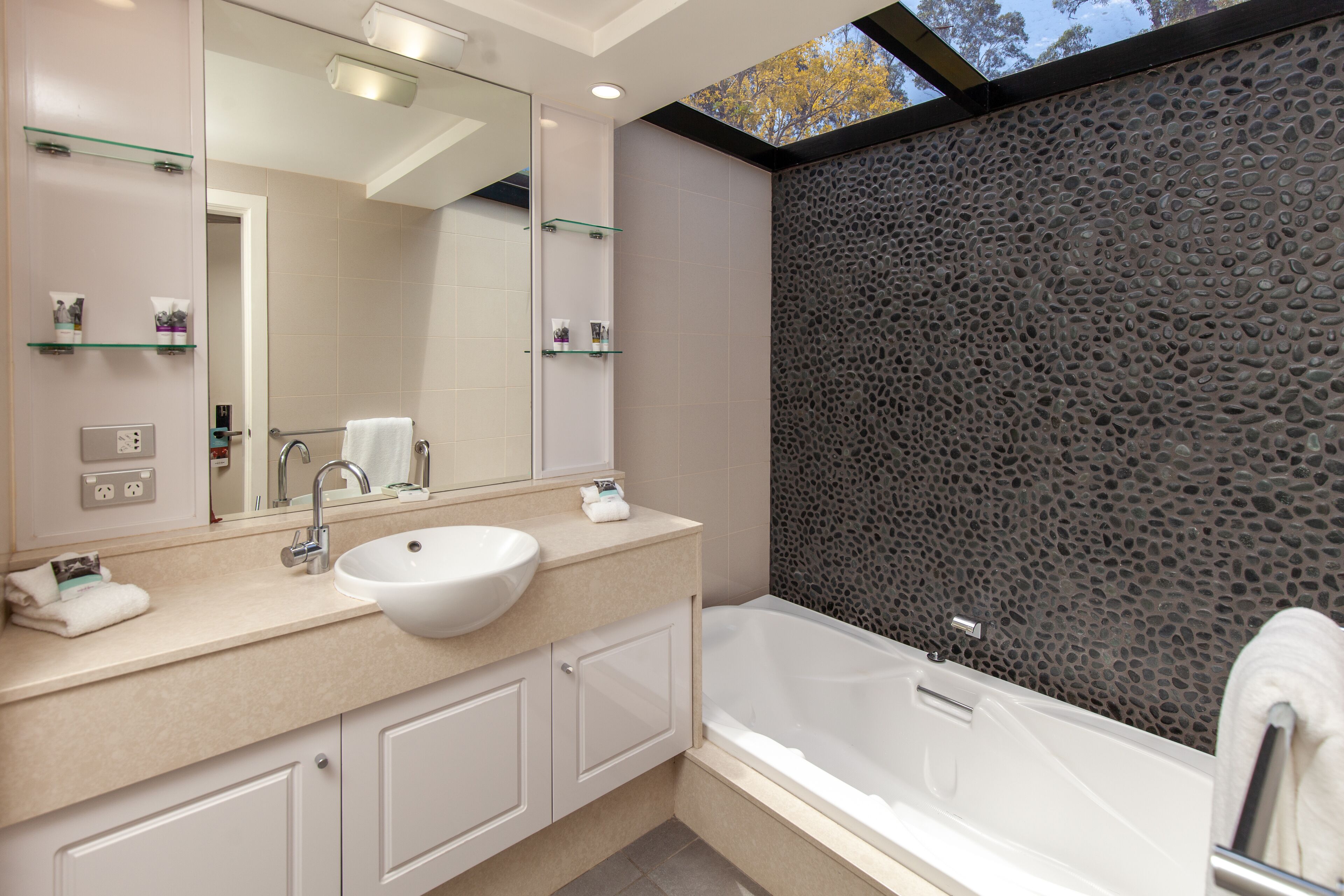 Un baño moderno con un lavamanos grande de color blanco, una bañera y una pared con textura de piedra.