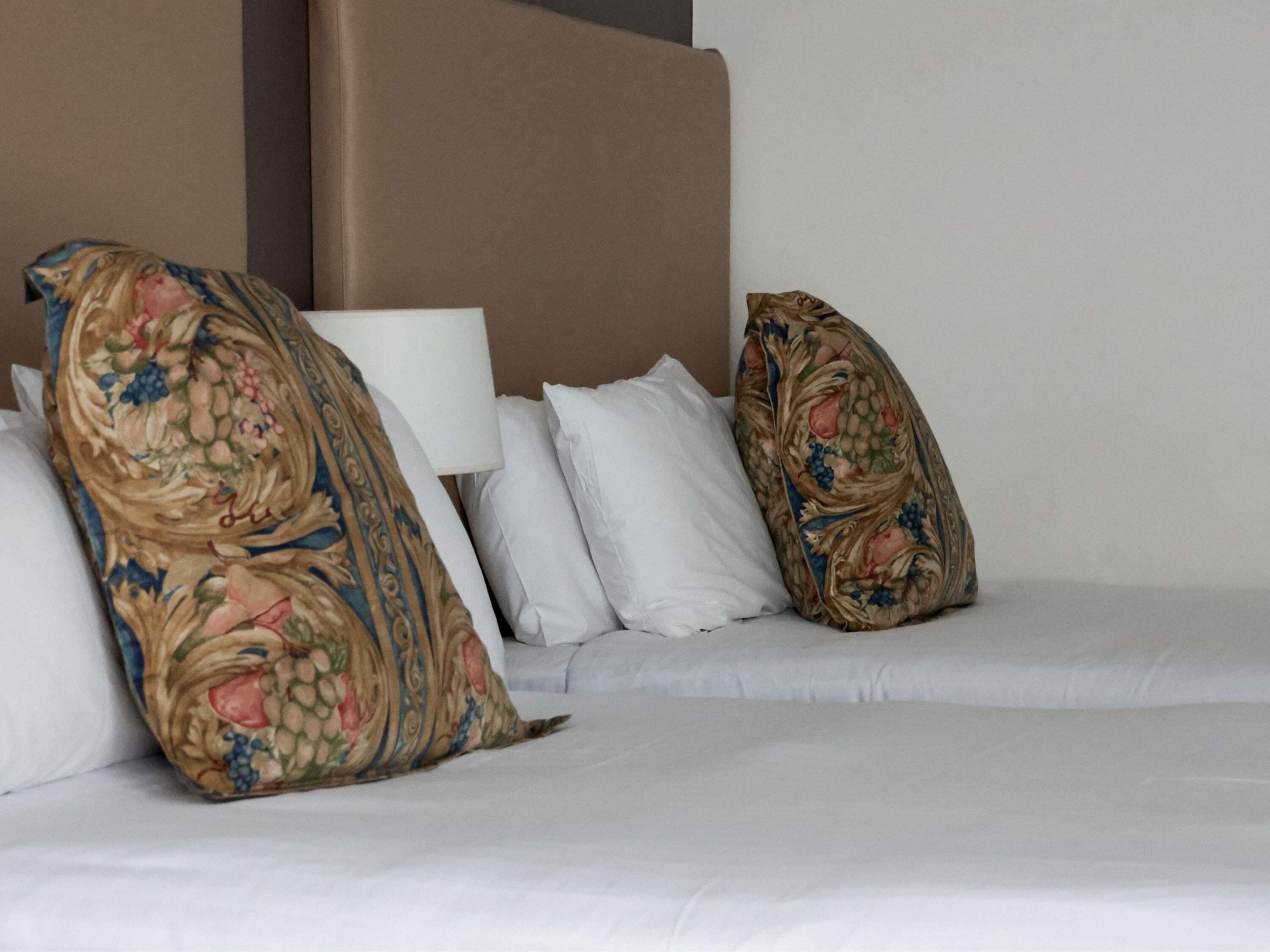 A bed with white bedding, two decorative pillows with a floral pattern, and a plain headboard.