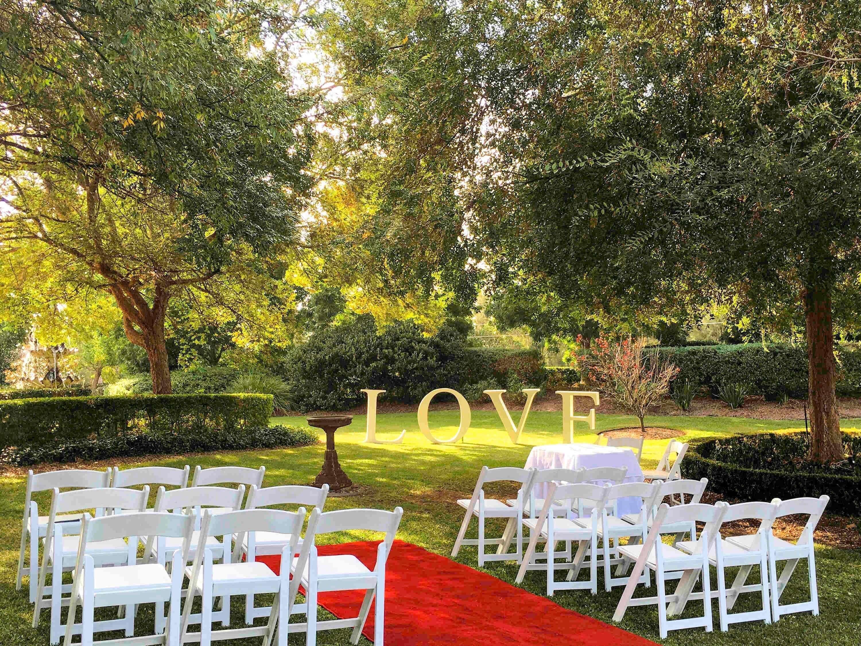 An outdoor venue with white chairs arranged in rows, a red carpet, and a large 'LOVE' sign.