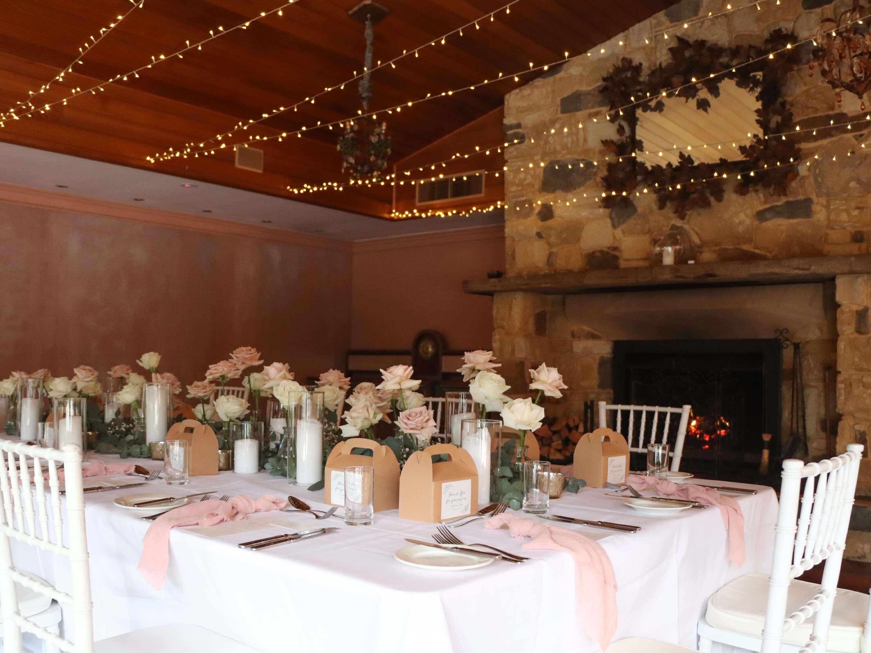 Een lange eettafel gedekt voor een formeel evenement, met witte tafelkleden, roze servetten en bloemstukken als decoratie.