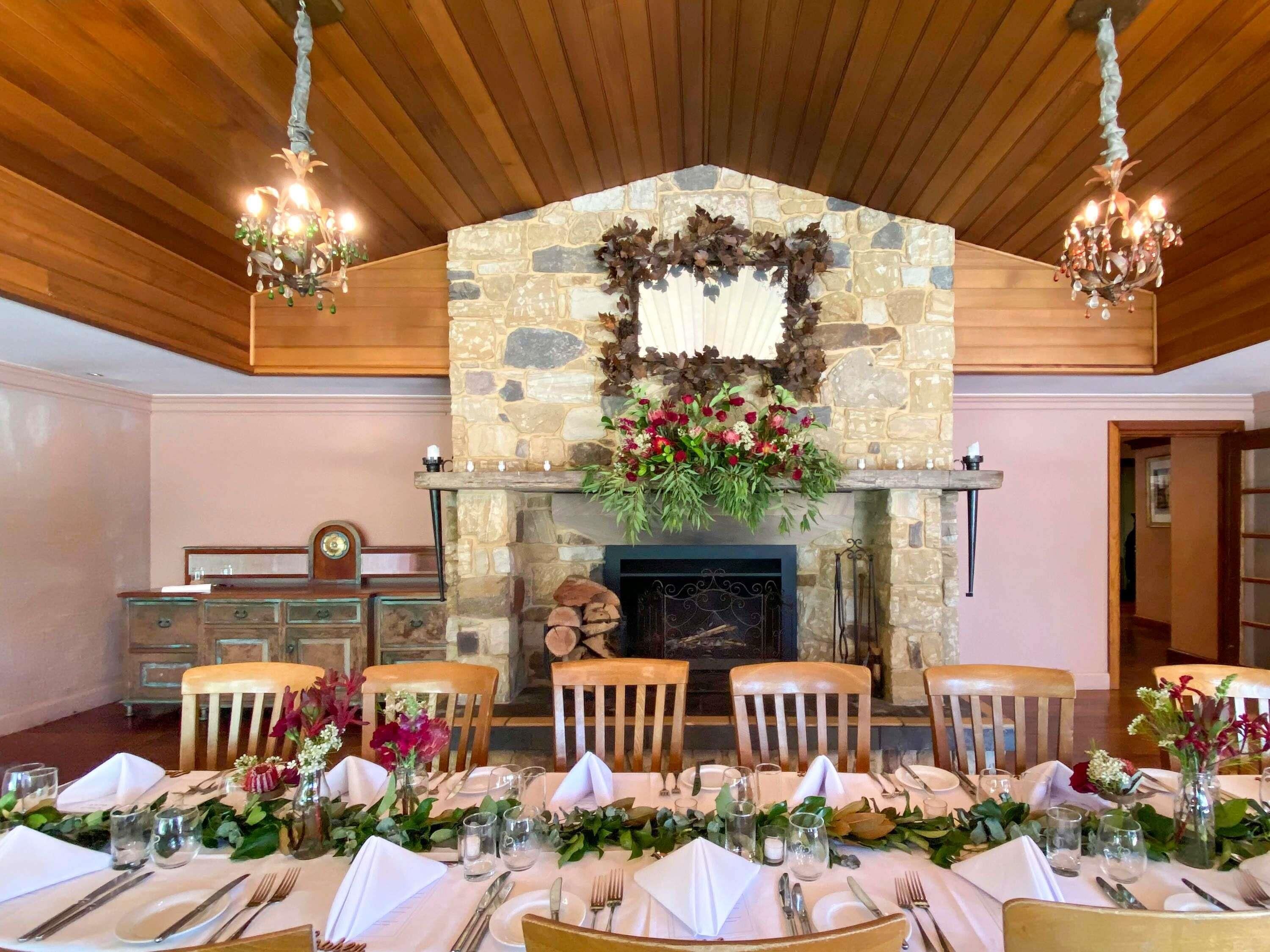 A dining area with a stone fireplace, wooden ceiling, and chandeliers.