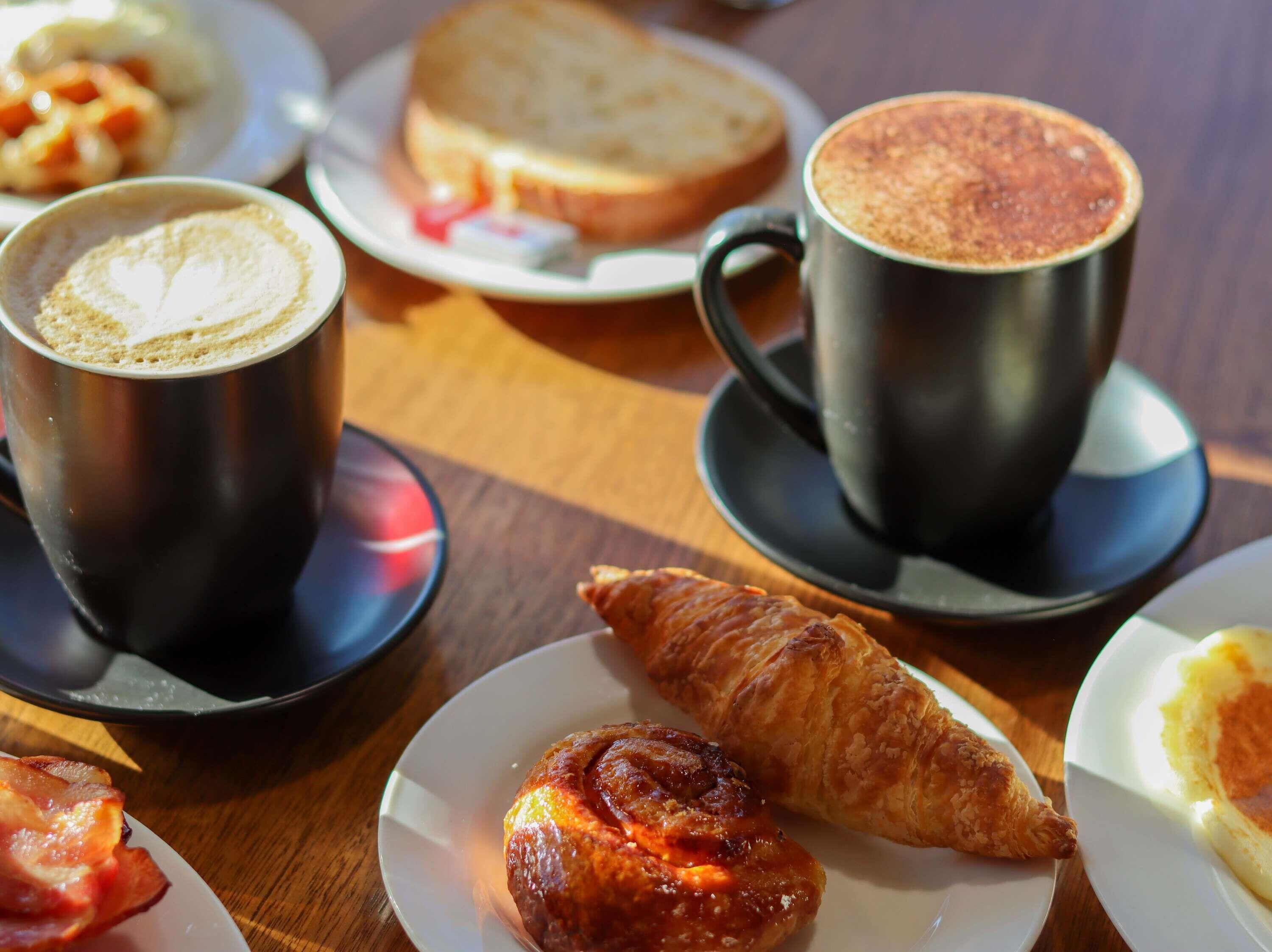 Una mesa con un croissant, una taza de café, una rebanada de pan y un plato con un pastel.
