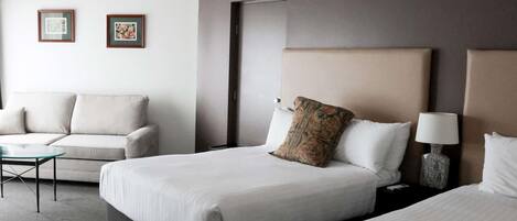A hotel room with two beds, a sofa, a small table, and two framed pictures on the wall.