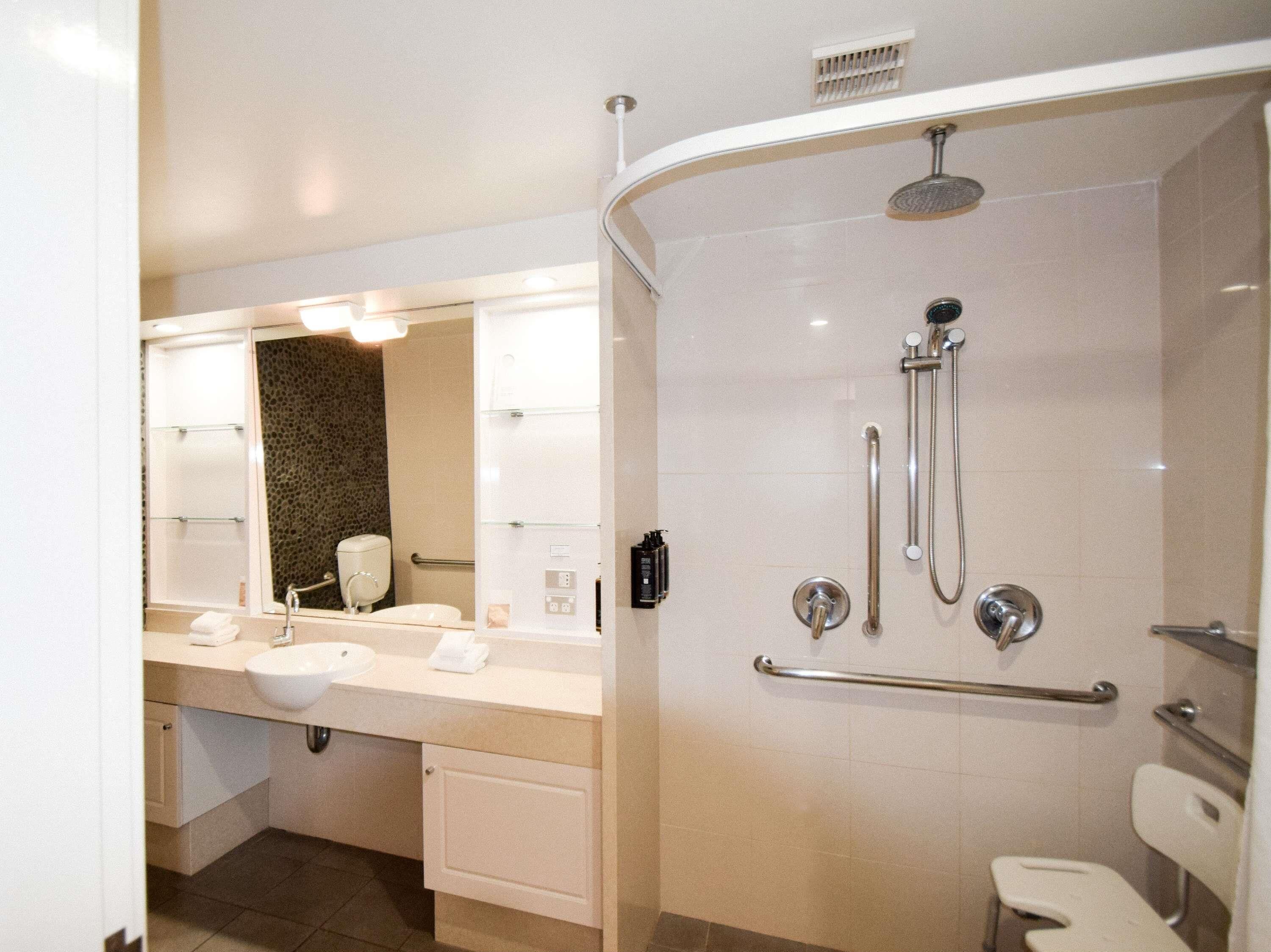 A modern bathroom with a curved shower, a large mirror, and a white sink.