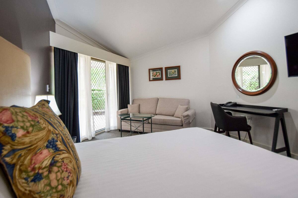 A hotel room with a bed, a desk, a chair, a sofa, a small table, and a window with curtains.