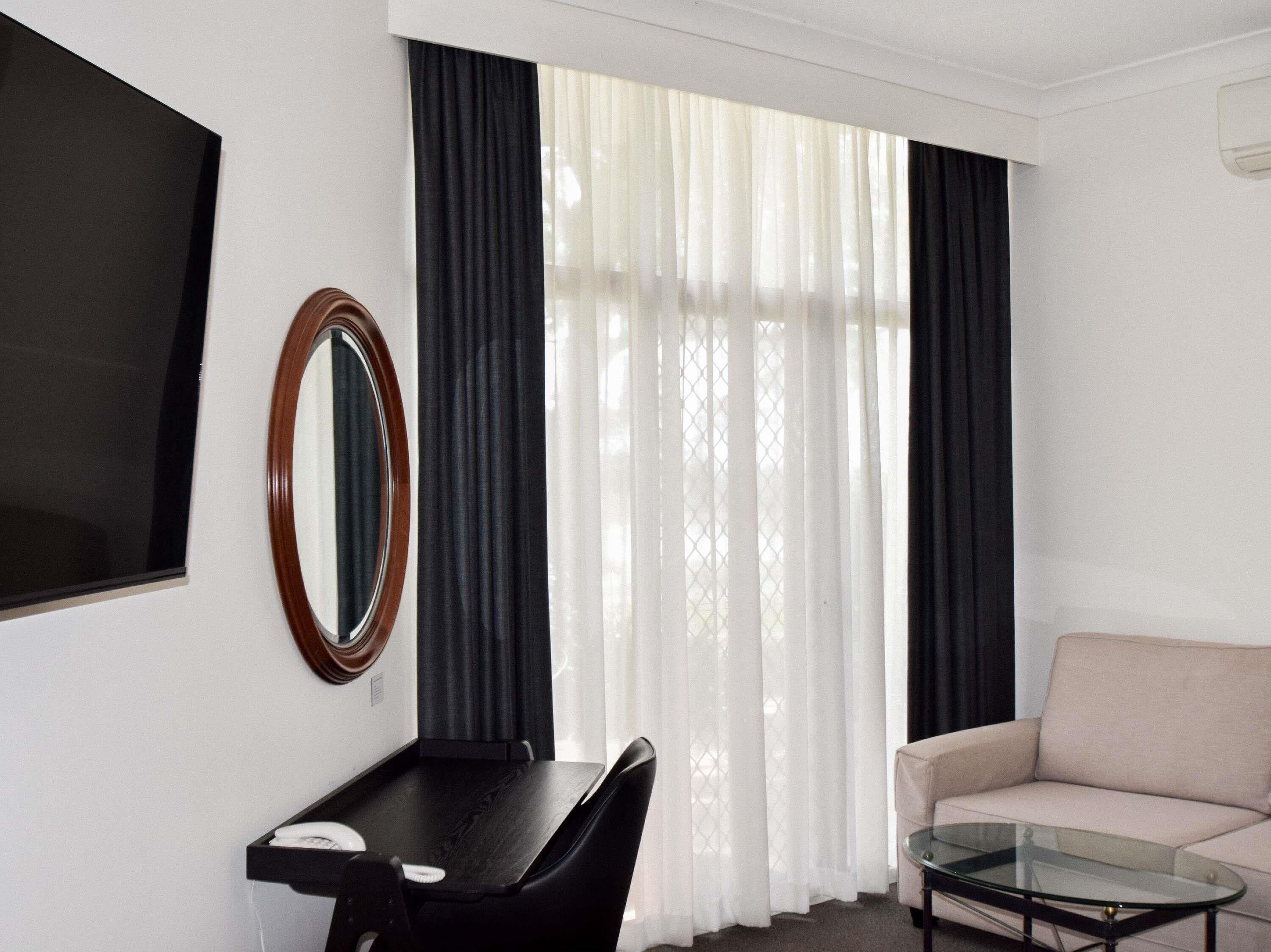 A room with a black desk, a round mirror, a beige sofa, and a glass coffee table.