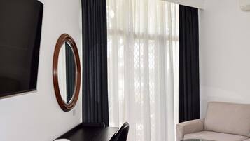 A room with a black desk, a round mirror, a beige sofa, and a glass coffee table.