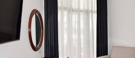 A room with a black desk, a round mirror, a beige sofa, and a glass coffee table.