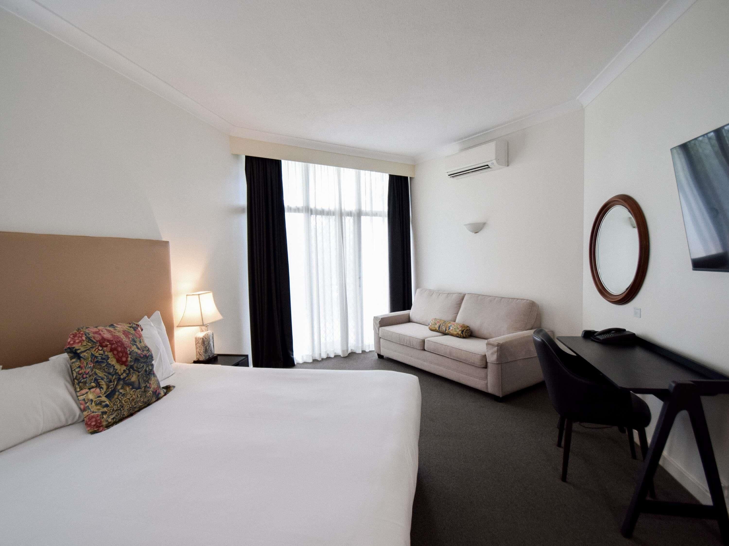 Habitación de hotel con cama, escritorio, sofá, televisor y aire acondicionado.