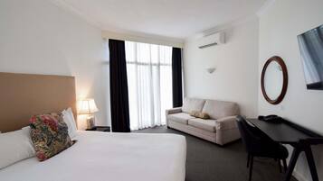 Habitación de hotel con cama, escritorio, sofá, televisor y aire acondicionado.