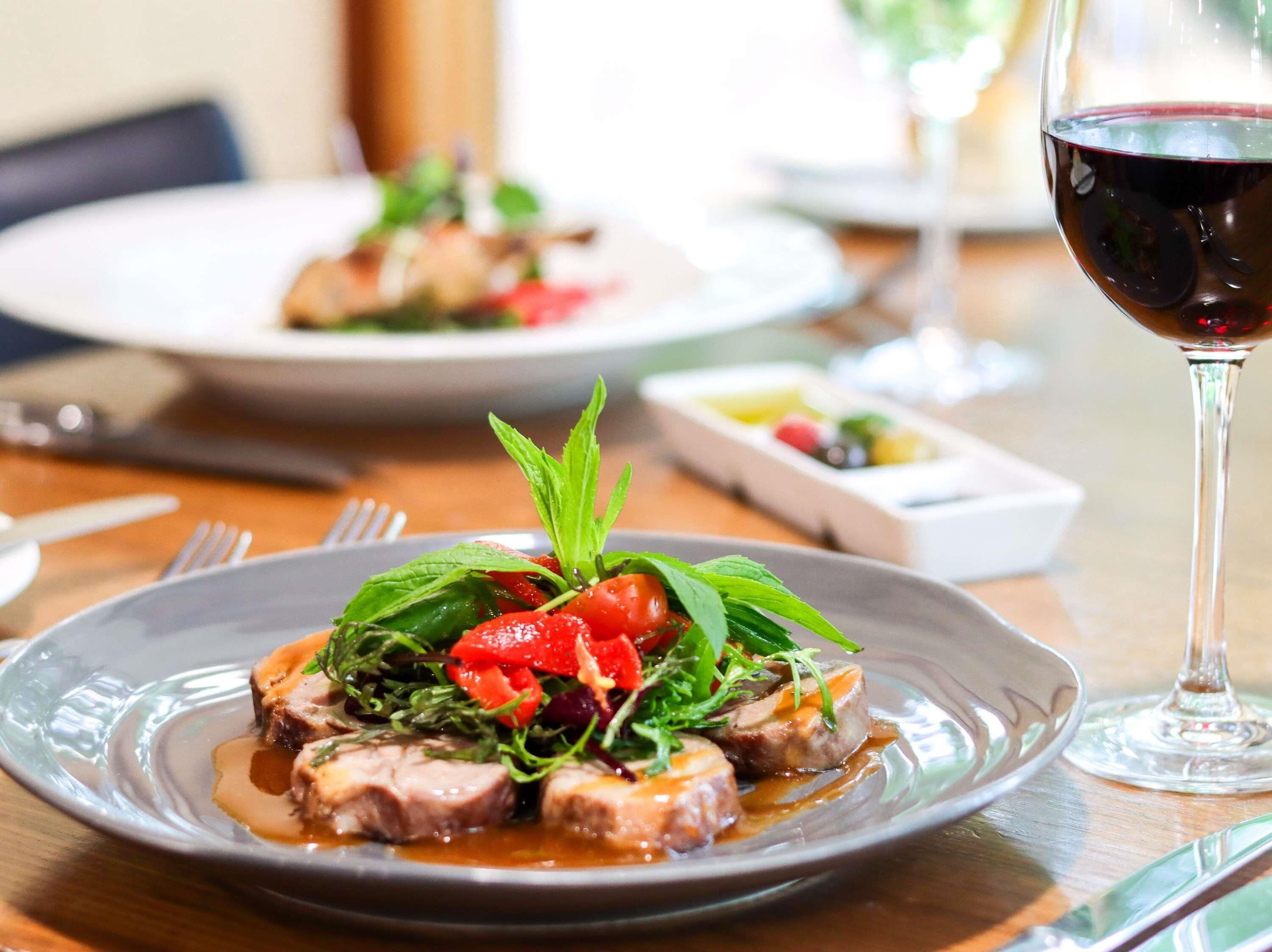 Una mesa de comedor con platos de comida, una copa de vino tinto y cubiertos.