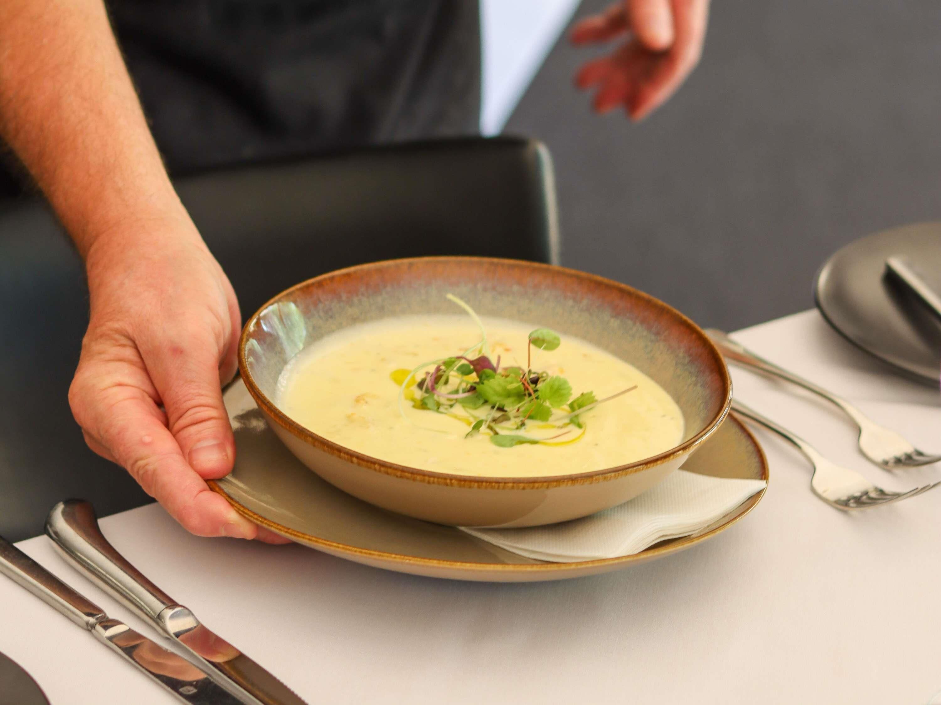 A person holding a bowl of soup with a spoon, placed on a plate.