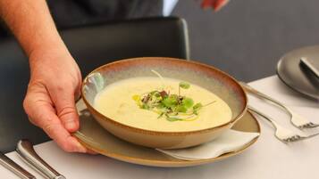 A person holding a bowl of soup with a spoon, placed on a plate.