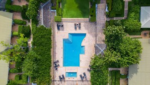 Vista aérea de un complejo turístico con una piscina central, rodeado de céspedes cuidados y senderos.
