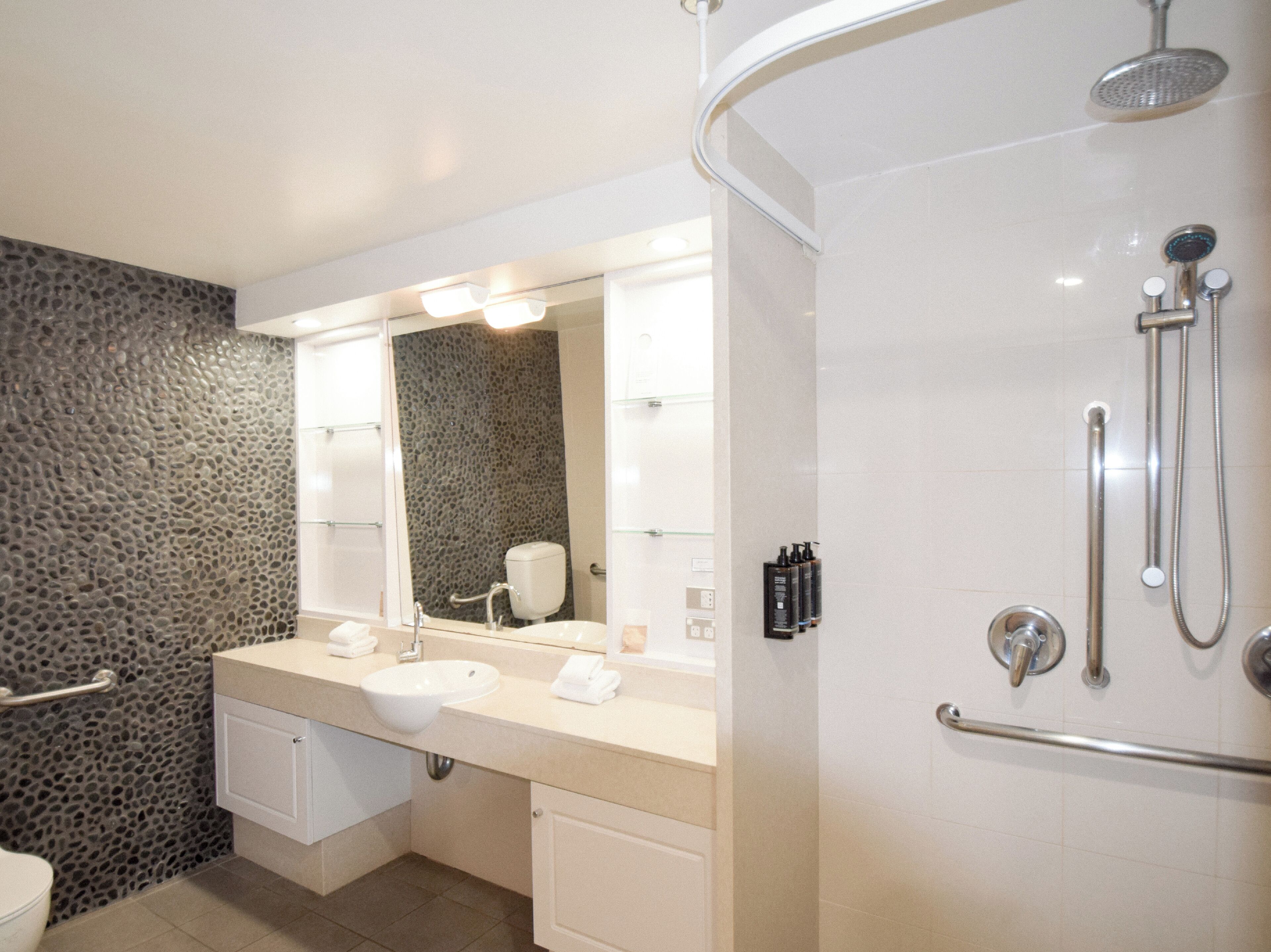 Un baño moderno con pared de piedra, un espejo grande, un lavamanos y una zona de ducha.