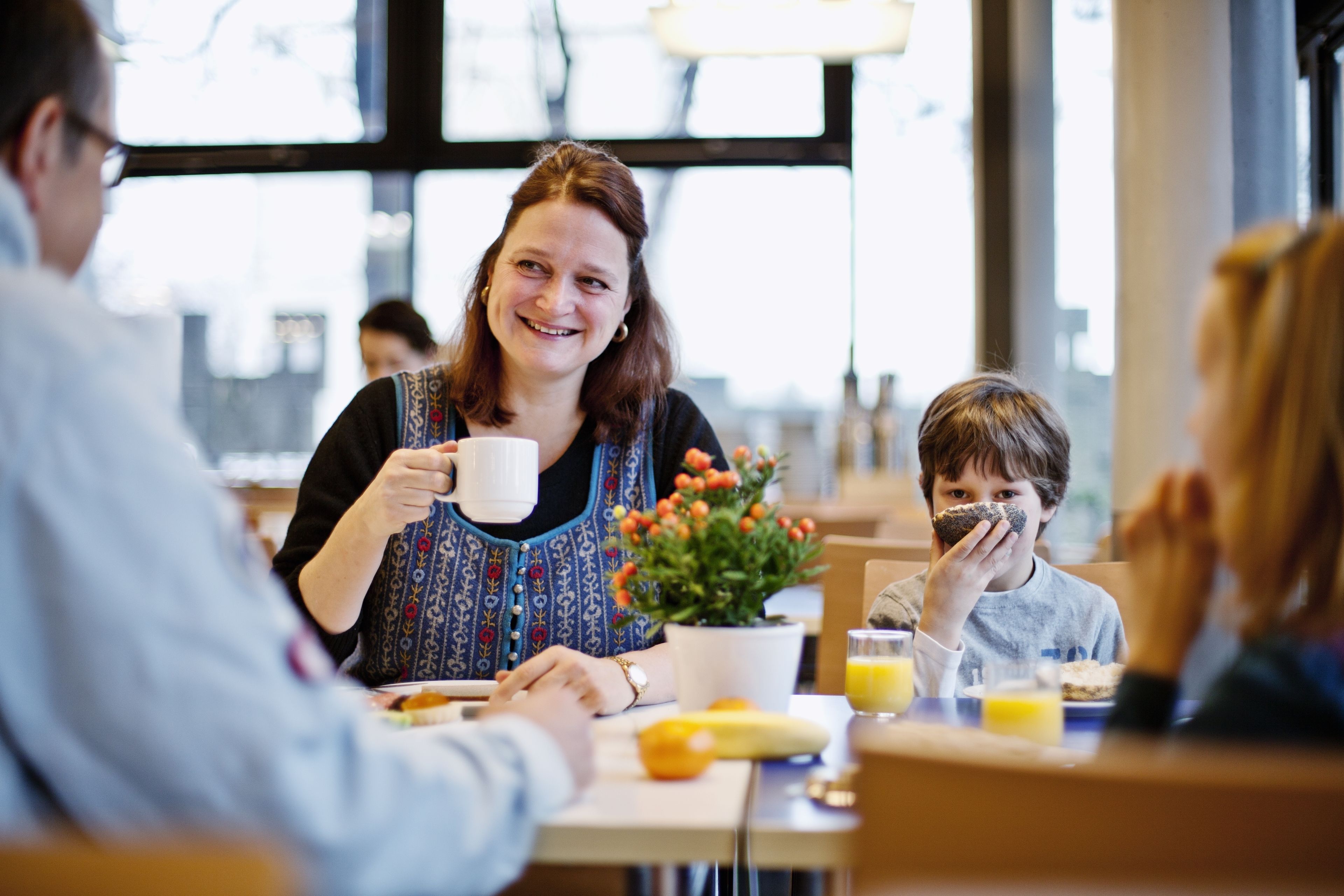 A family dining at a table with a potted plant, a banana, and a glass of orange juice.