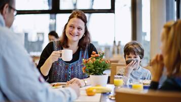 A family dining at a table with a potted plant, a banana, and a glass of orange juice.
