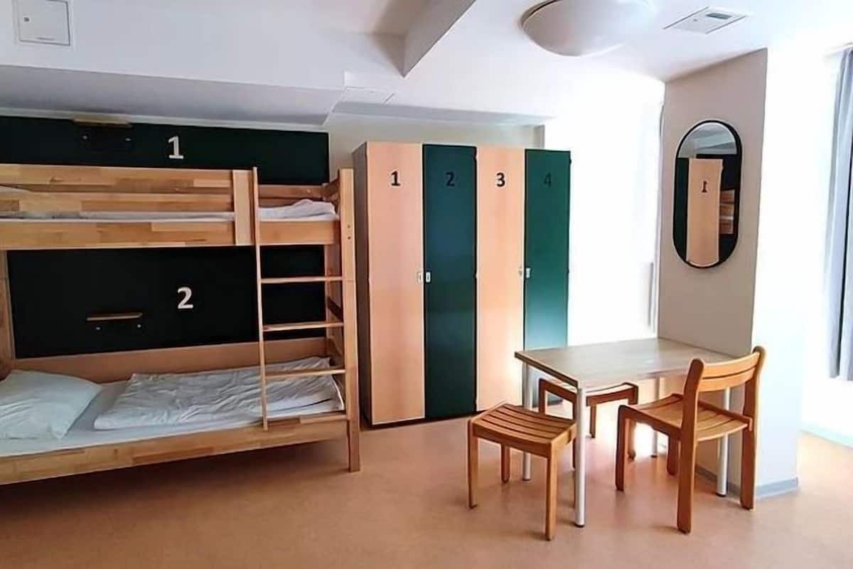 A dormitory room with bunk beds, a desk, chairs, and lockers.