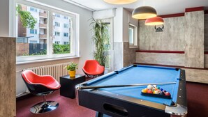 A pool table in a modern room with large windows, red chairs, and pendant lights.