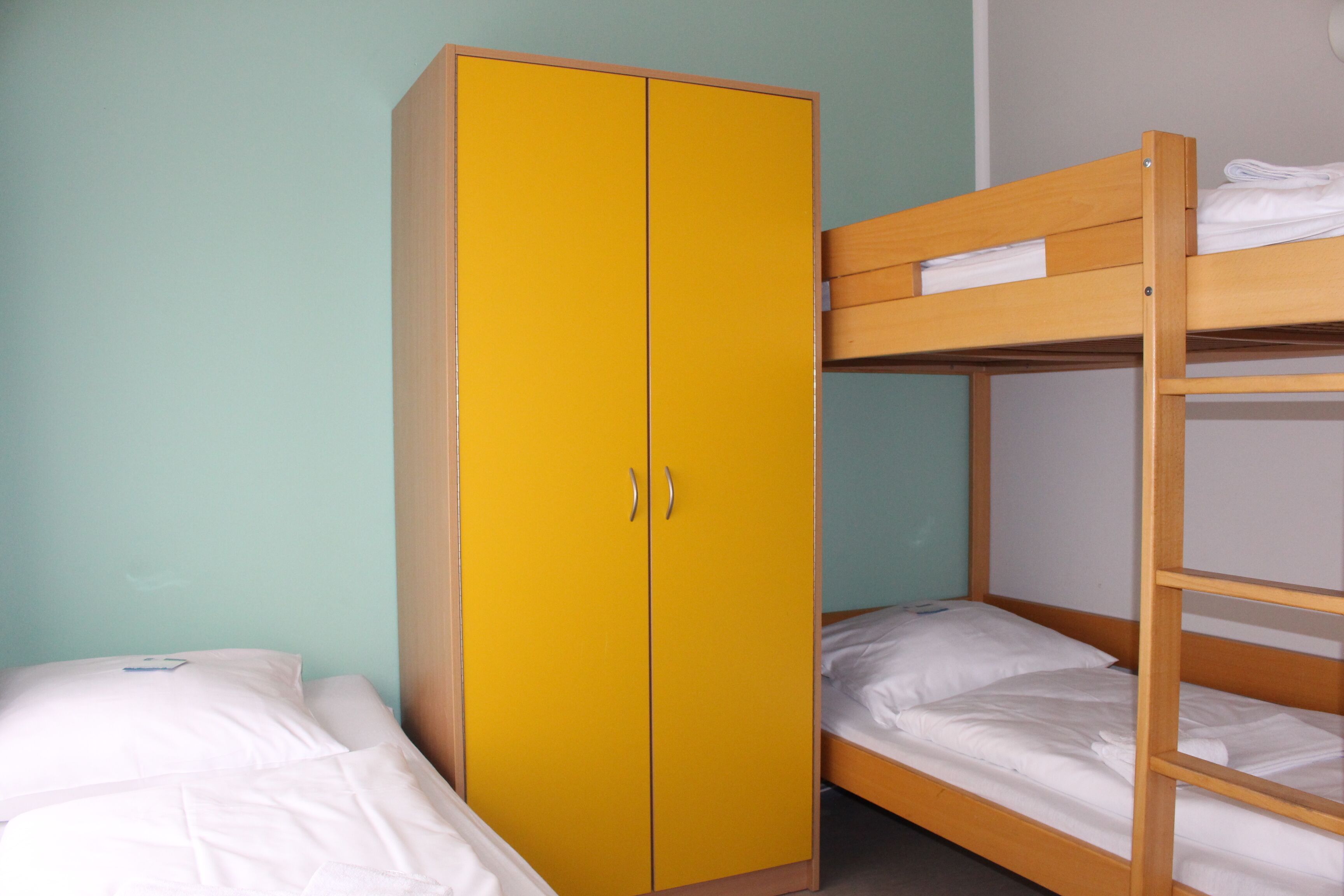 Una habitación con literas, un armario amarillo y una cama individual.