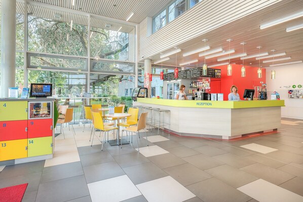 A modern reception area with a bright red counter, yellow chairs, and a large window providing natural light. - martas Gästehäuser Hauptbahnhof Berlin - Hostel (Berlin)