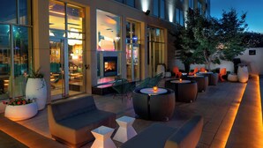 An outdoor seating area with modern furniture, a fireplace, and large windows. - Aloft by Marriott Rogers-Bentonville (Rogers)