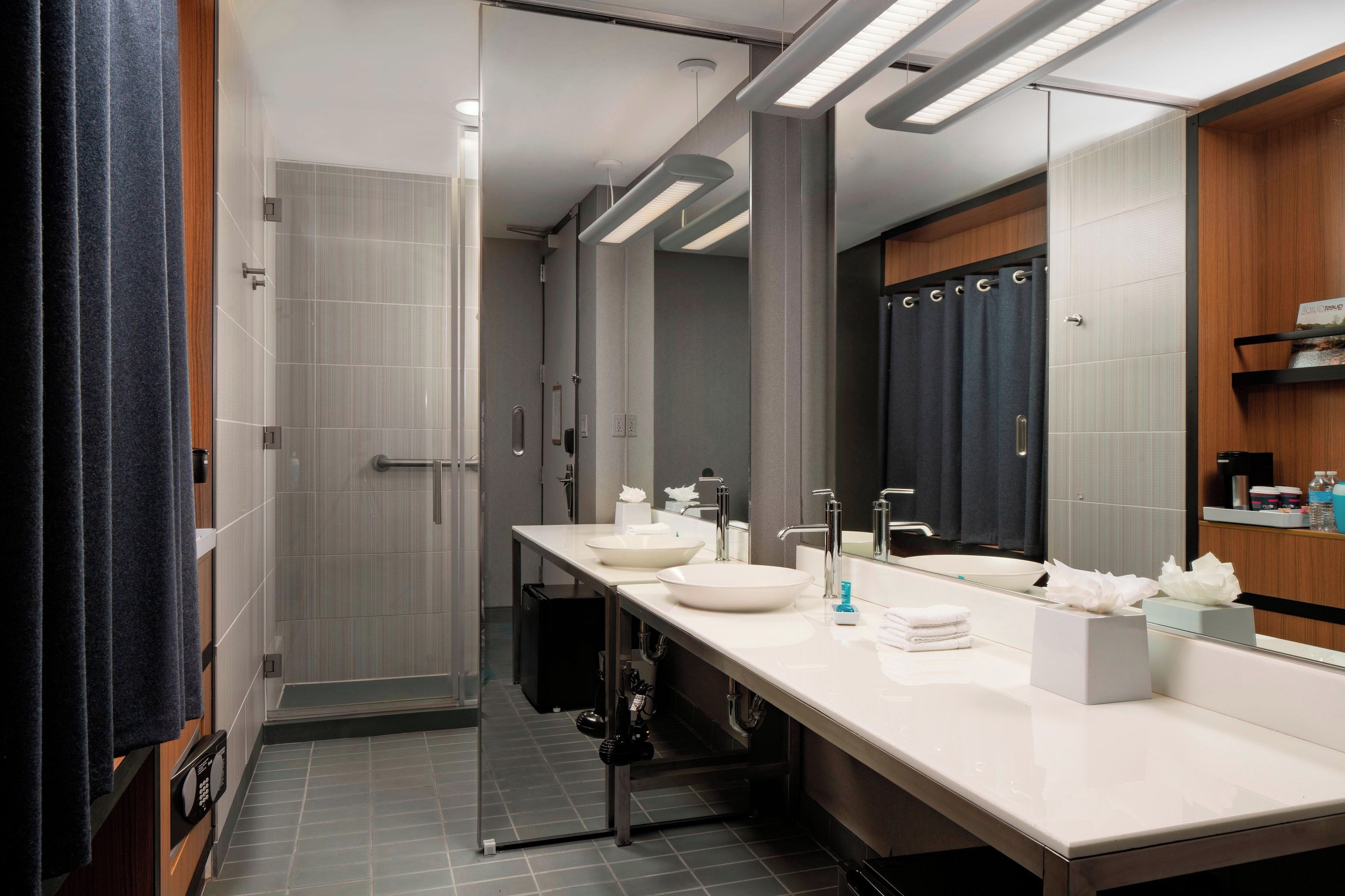 Une salle de bain moderne avec un long meuble-lavabo, deux vasques, un grand miroir et un espace douche.