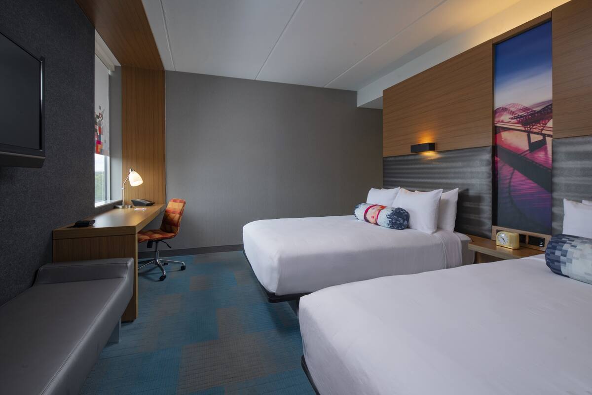 A hotel room with two beds, a desk, a chair, and a large window.