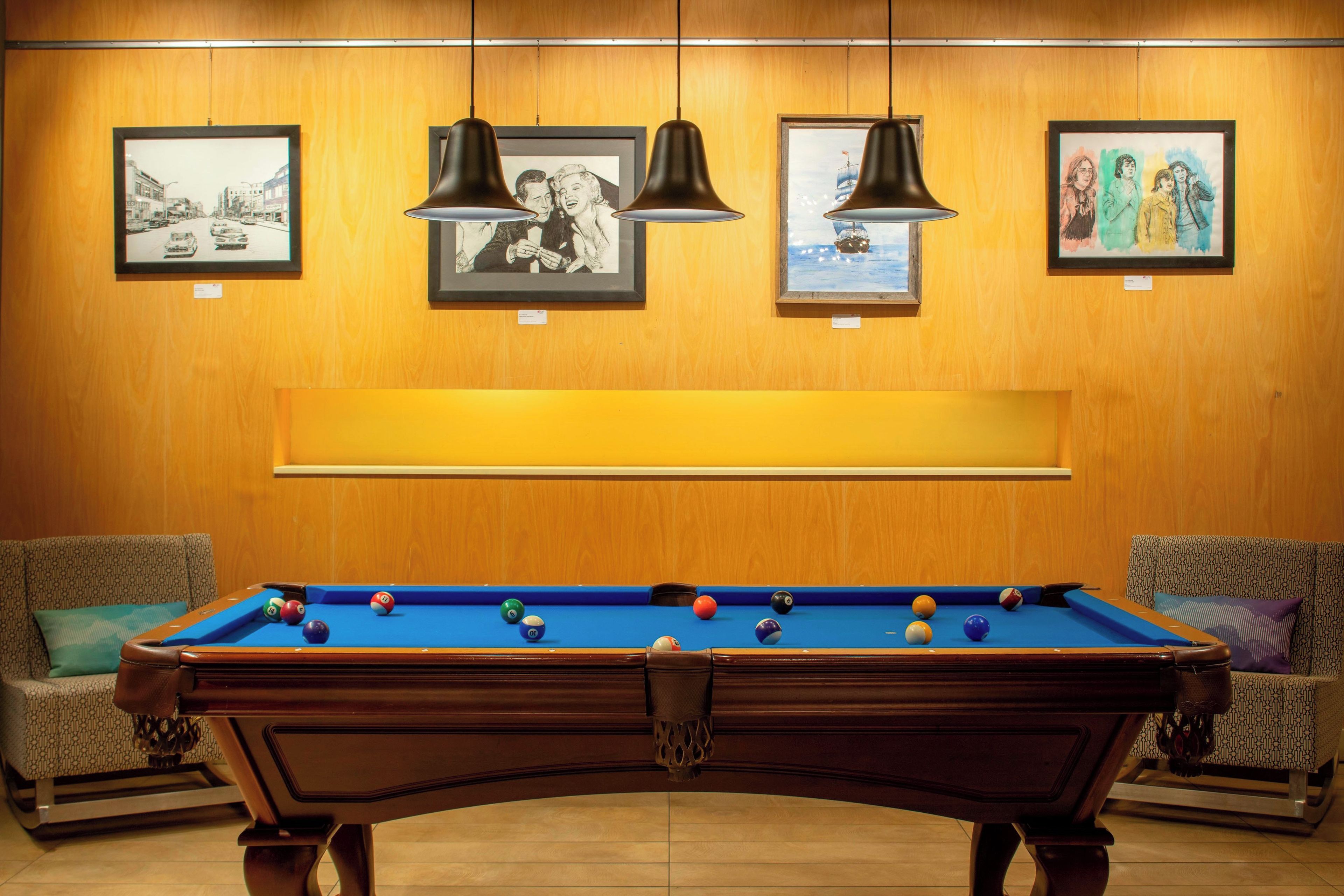 A pool table with balls, surrounded by two sofas, and framed artworks on the wall.