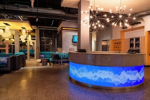 A modern reception area with a curved counter, a digital sound wave display, and a starry light fixture. - Aloft by Marriott Rogers-Bentonville (Rogers)
