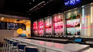 Een bar met een neonbord, een digitaal scherm en een rij stoelen.