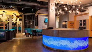 A modern reception area with a curved desk, a digital sound wave display, and a starry ceiling light fixture. - Aloft by Marriott Rogers-Bentonville (Rogers)