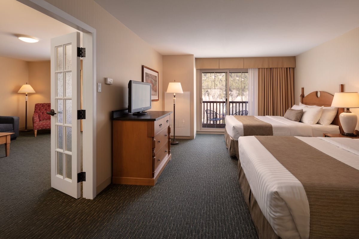 A hotel room with two beds, a desk with a computer, a dresser, and a balcony with curtains.