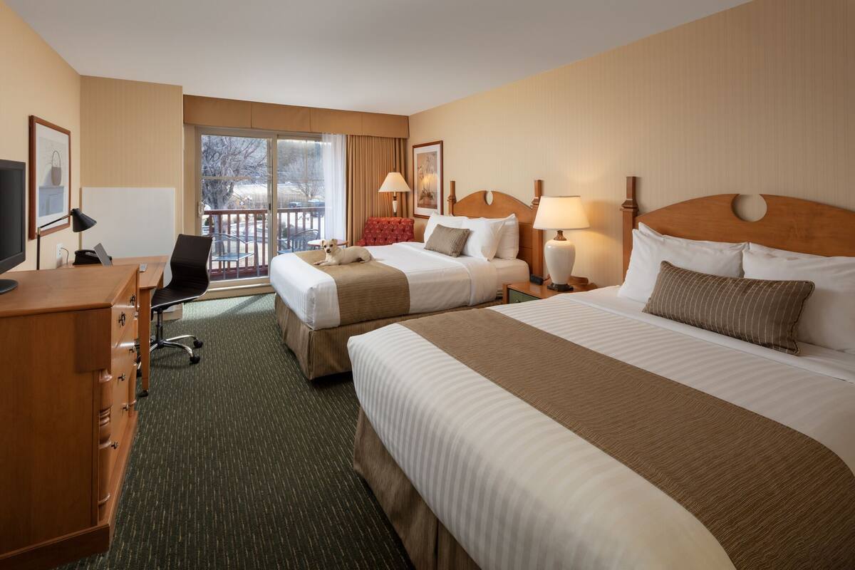 A hotel room with two beds, a desk, a chair, a TV, and a balcony with a view.