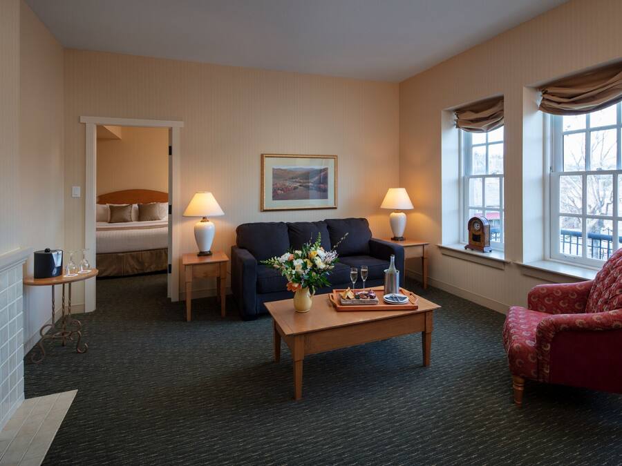 A hotel room with a sofa, armchair, coffee table, and a fireplace.
