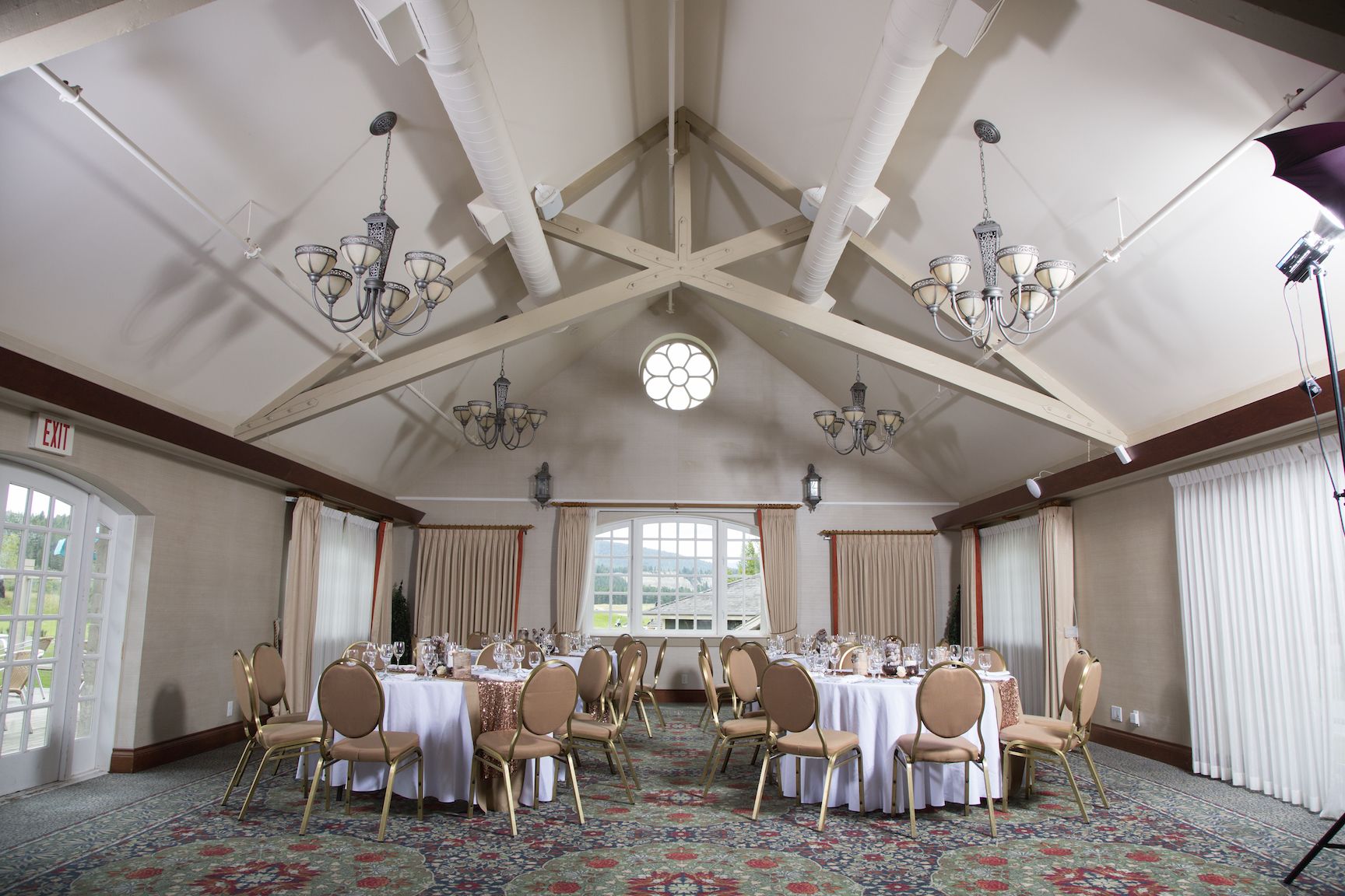 Une salle de banquet avec de hauts plafonds, des lustres et de grandes fenêtres. Les tables sont dressées pour un événement formel.