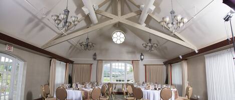 Une salle de banquet avec de hauts plafonds, des lustres et de grandes fenêtres. Les tables sont dressées pour un événement formel.