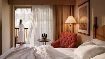 A hotel room with a bed, a red armchair, a standing lamp, and a framed picture on the wall.