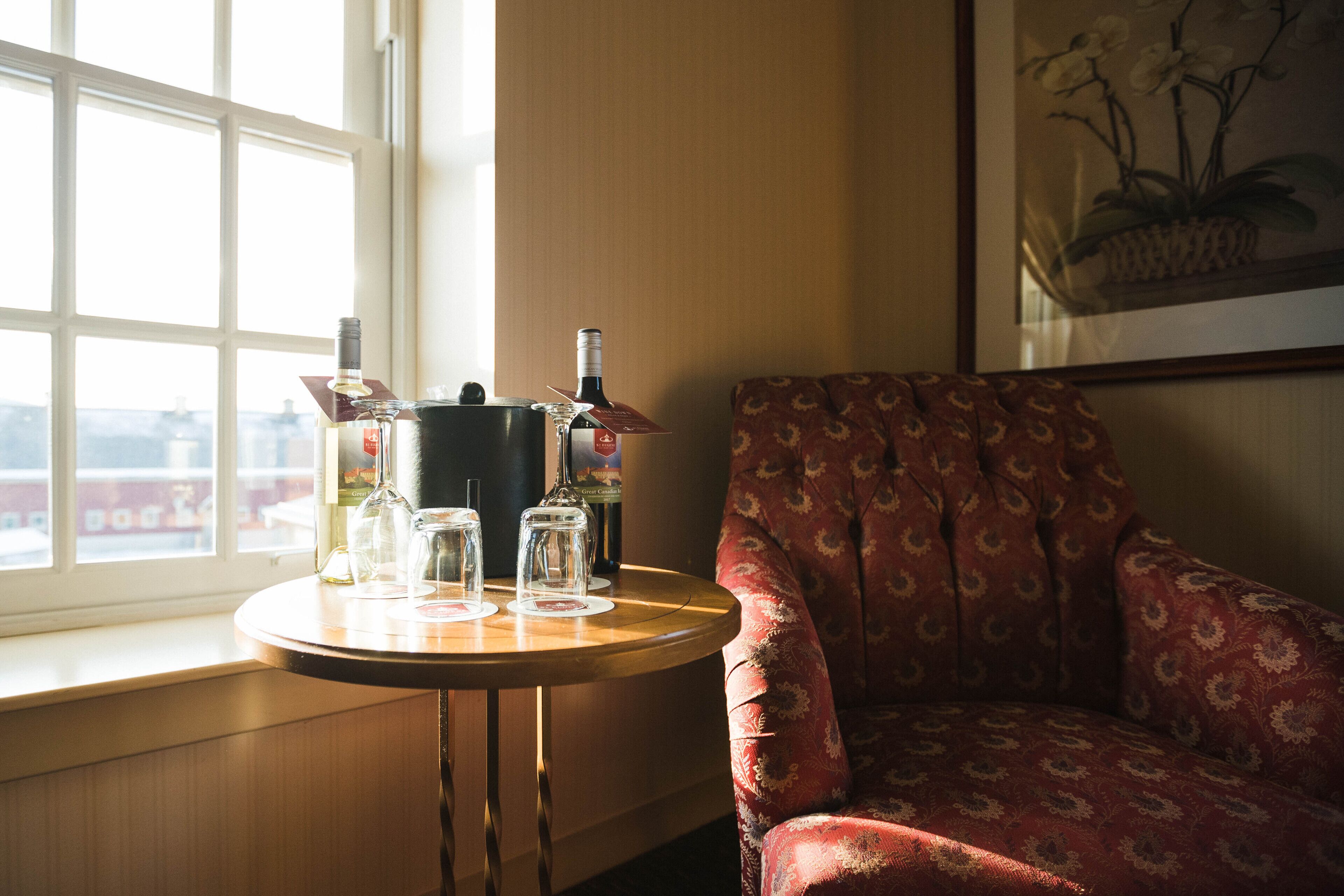 A room with a window, a table with glassware and bottles, and a patterned armchair.