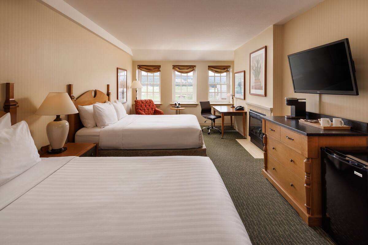 A hotel room with two beds, a desk, a chair, a television, and a coffee maker.