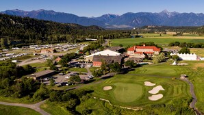 Une vue aérienne d’un complexe hôtelier comprenant un terrain de golf, un grand bâtiment avec un toit rouge et des montagnes en arrière-plan.